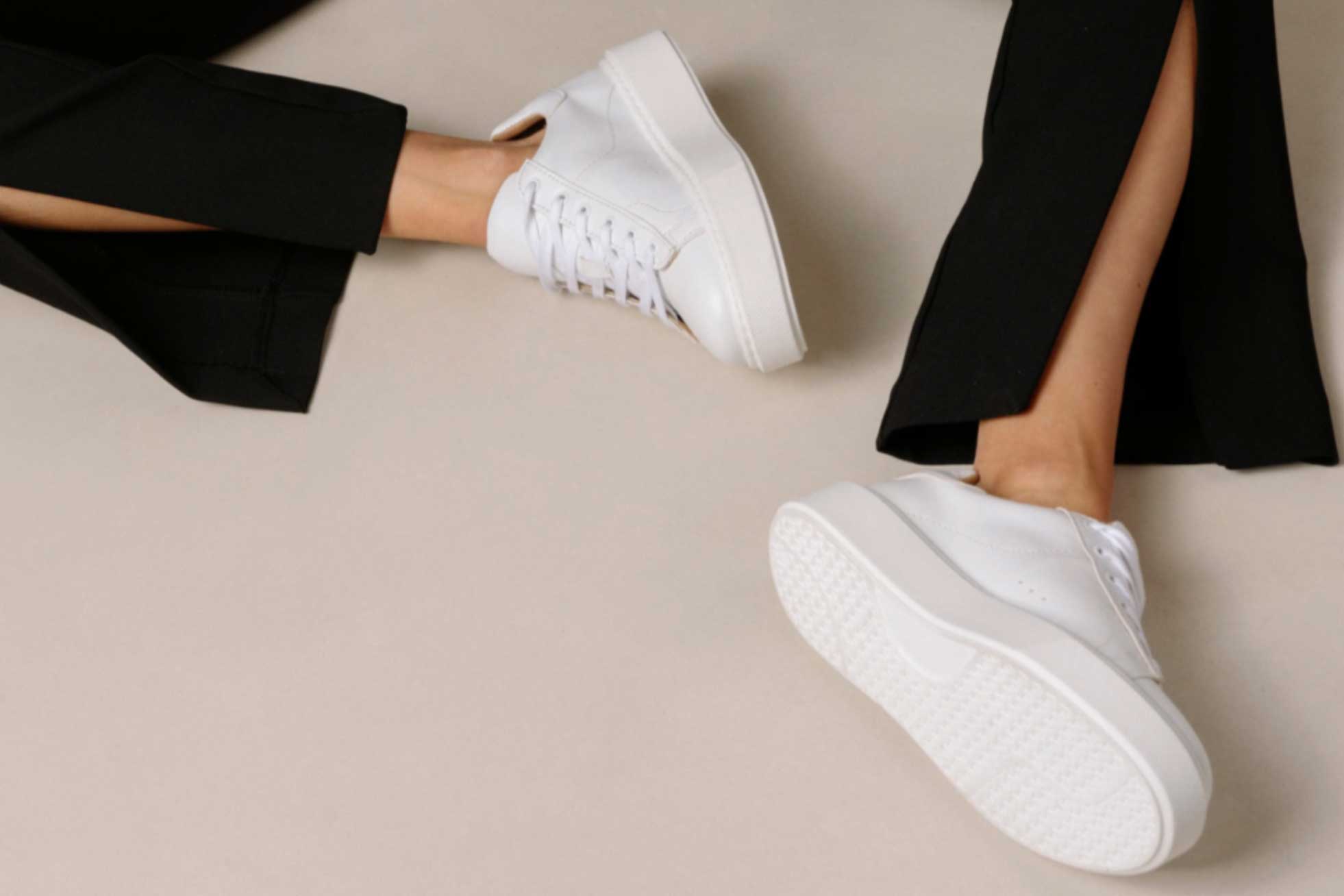 A woman sits on the ground wearing white Aloha sneakers and black pants.