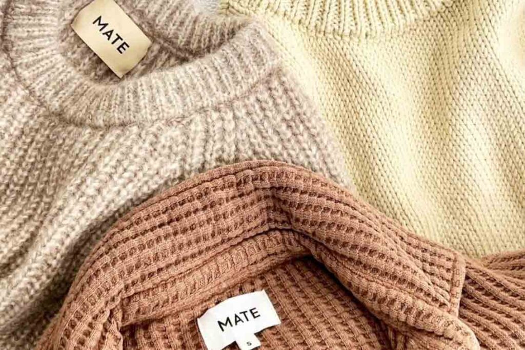 Set of three MATE the Label Sustainable Sweaters made of organic cotton, in brown, tan, and yellow, with white MATE the Label tags.
