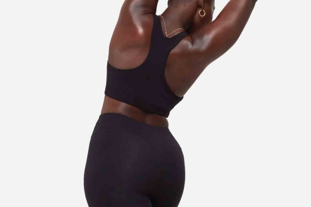 Woman leans to the right with hands extended over head. She wears black MATE the Label sports bra and leggings/