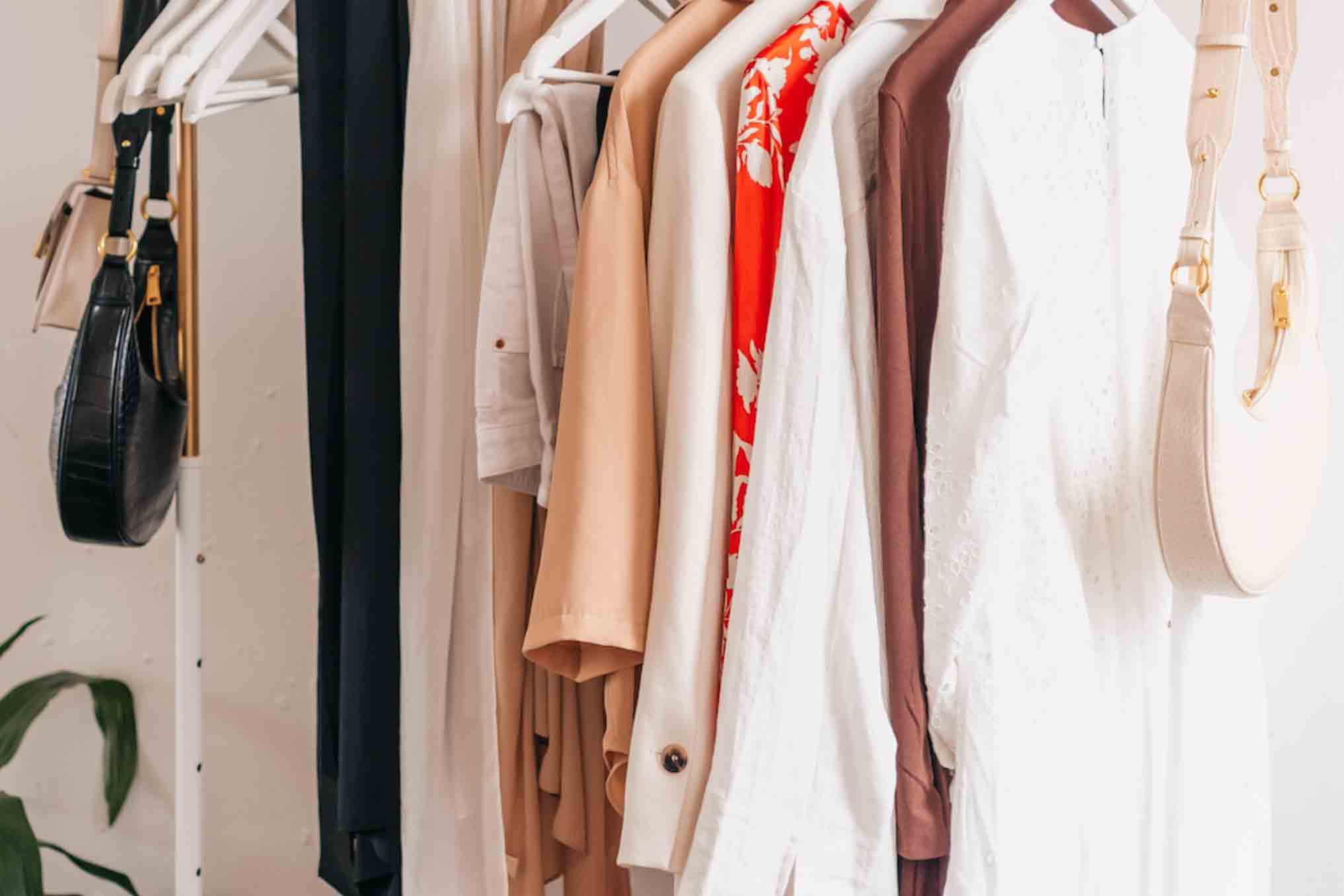 A clothing rack holding sustainable wardrobe clothing, including white red, and brown cotton shirts.