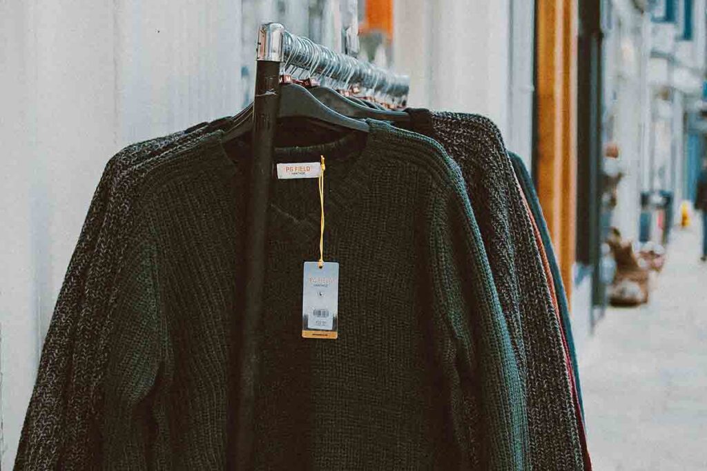 Fast Fashion vs Sustainable fashion clothing hanging on a clothing rack. A black sweater is shown on top with a white tag
