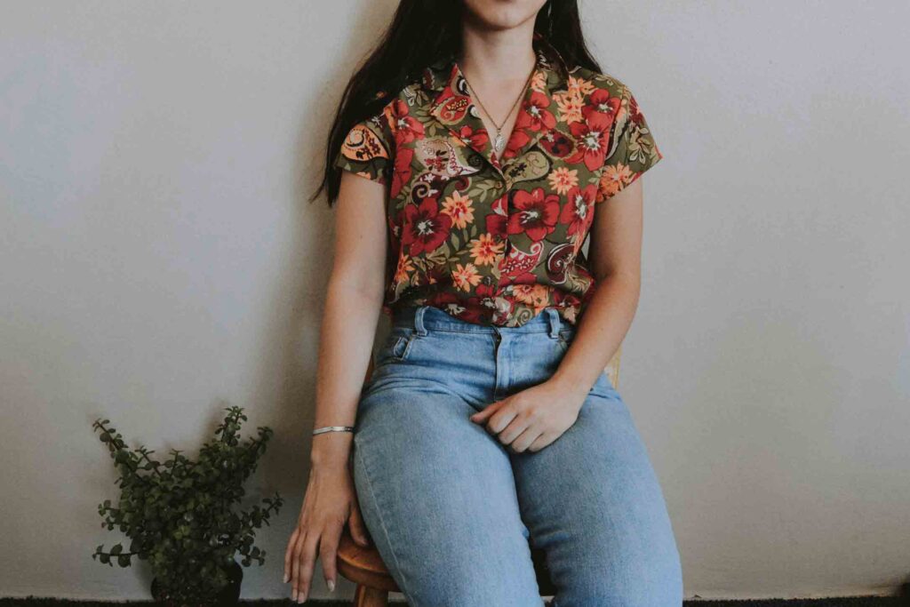 A woman wears a red button down shirt and blue jeans. 