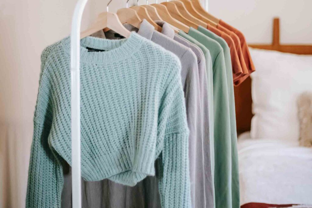 A rack of colorful sweaters against a white wall.