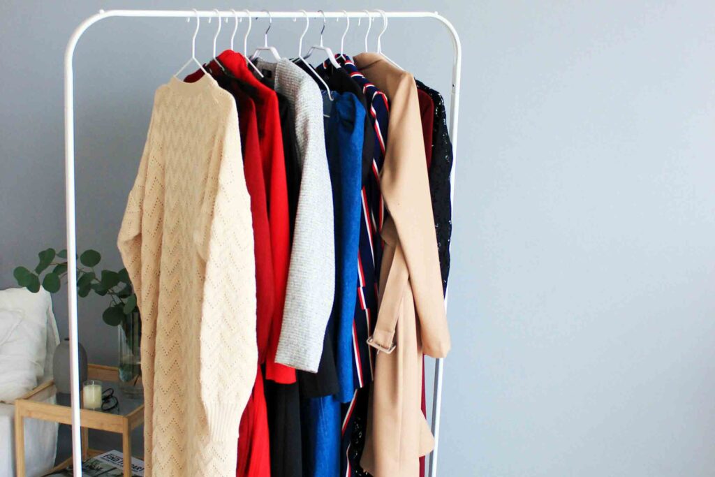 A sustainable wardrobe hangs on a clothing rack in front of a blue wall.