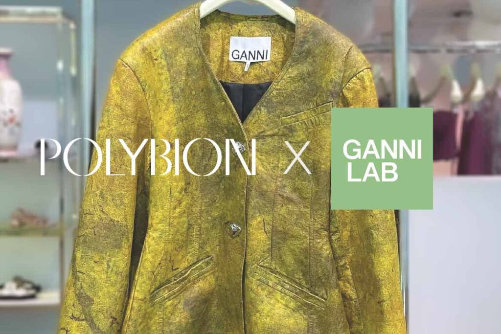 A yellow jacket made from Polybion's cellulose is shown off inside Ganni's flagship store in Copenhagen. It hangs on a white hanger. Text on the image reads "Polybion x Ganni Lab."