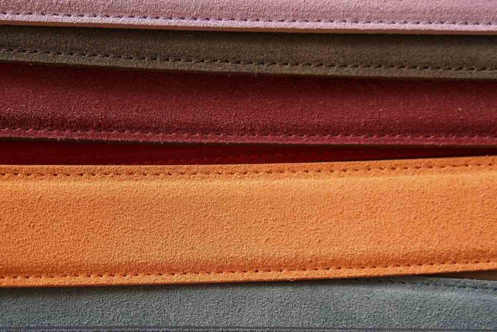 A stack of leather in different colors, including red, orange, gray, pinkn, red and brown. 