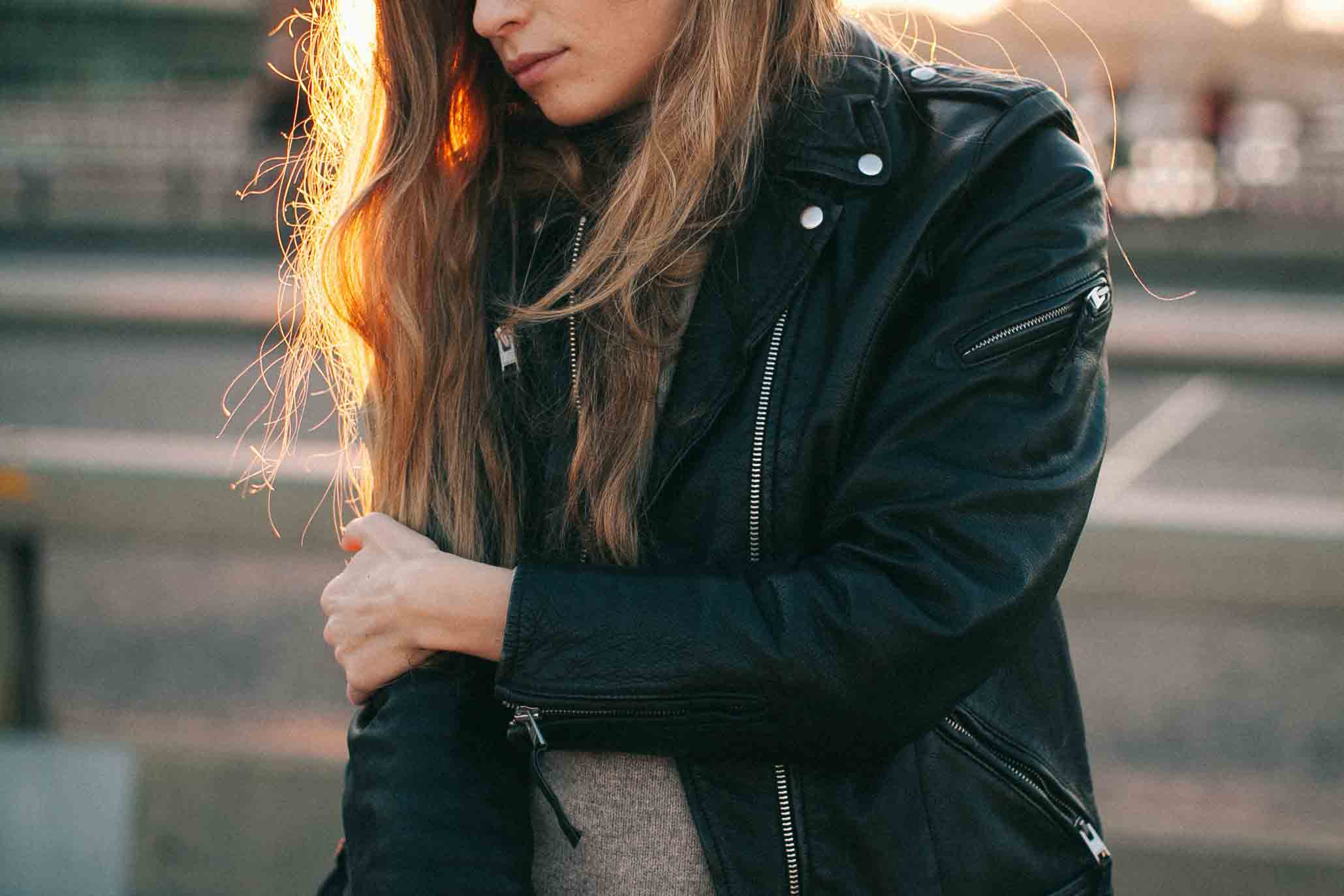 A woman wears a black leather jacket and has her right arm crossed over her left.