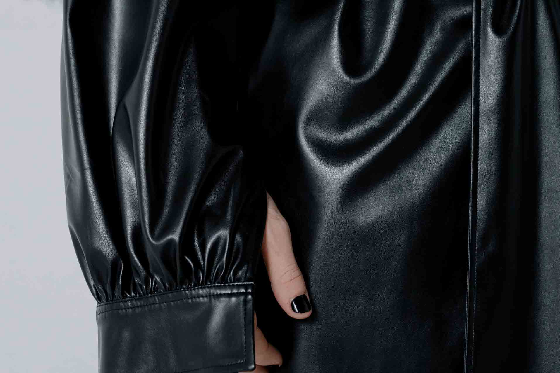 A close up of a woman's arm wearing a black baggy vegan leather jacket.