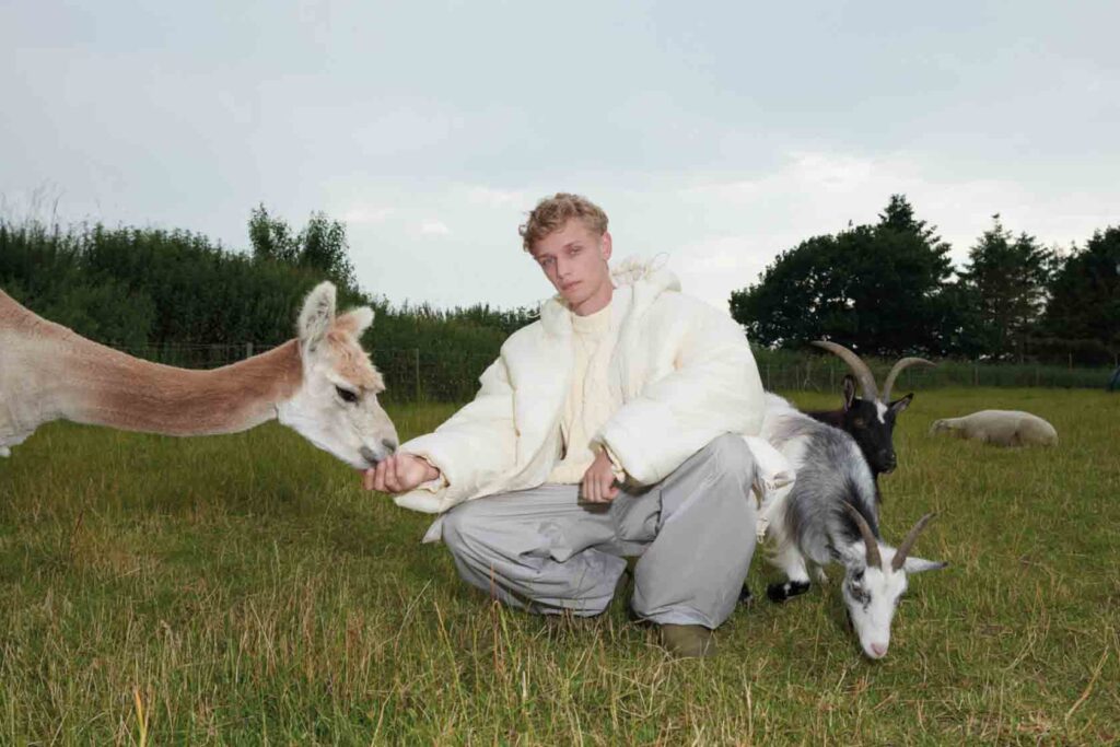 A model from H&M's collection, wearing white shirt and crouched by two goats.