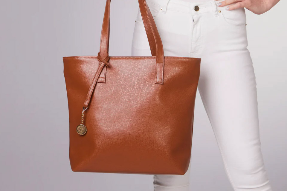 A woman in white pants holds a brown vegan leather bag made from MIRUM