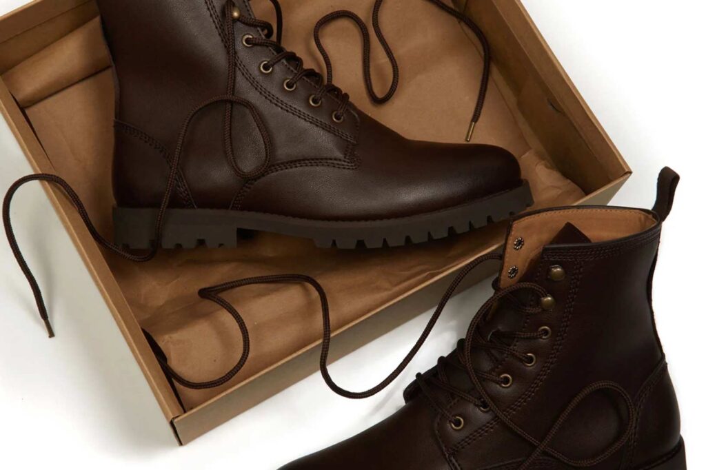 Brown vegan leather boots lay on a brown box and white background