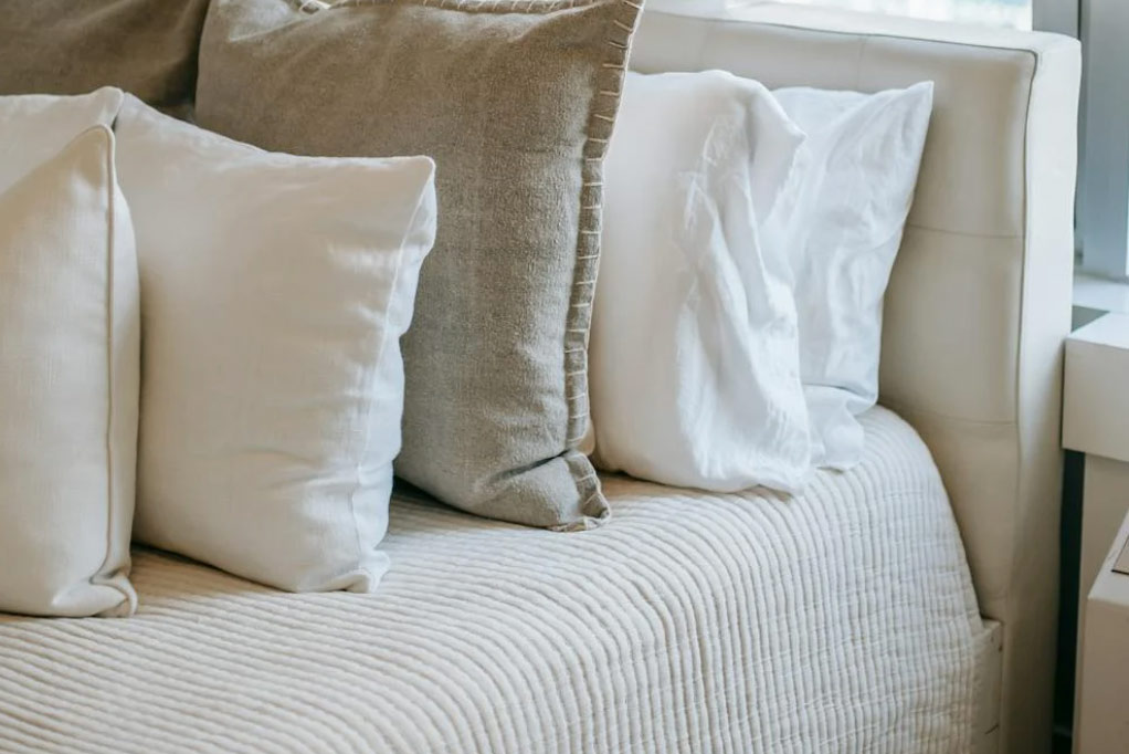 A simple bed layout with white and tan linen and cotton sheets.