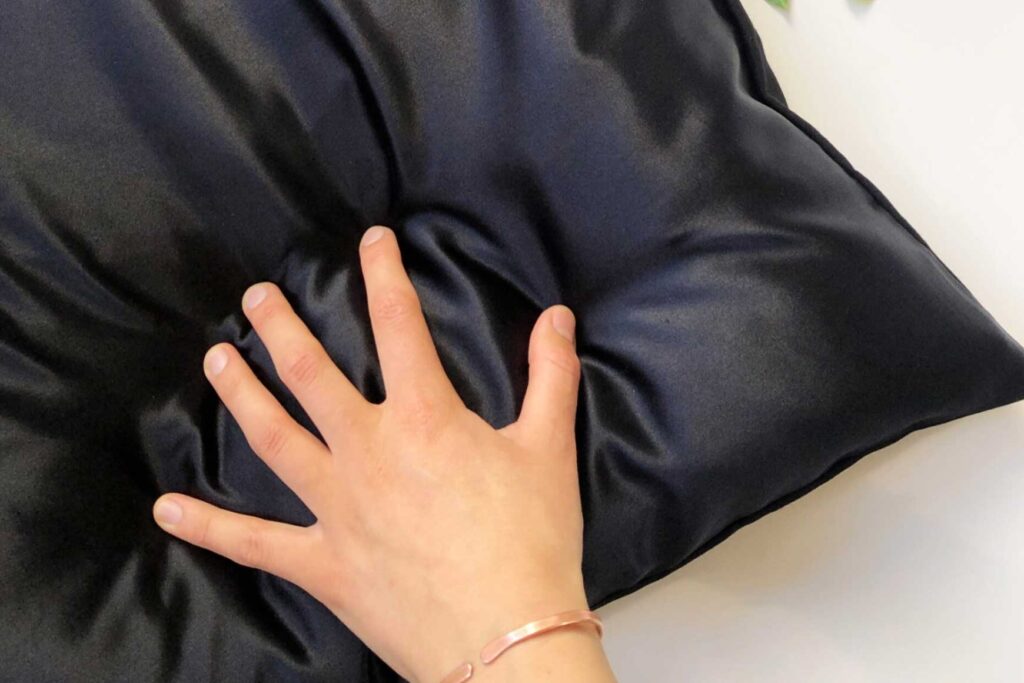 A hand sits on top of a charcoal gray silk pillow case